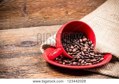 Red coffeecup and plate with spilled coffeebeans on gunny background