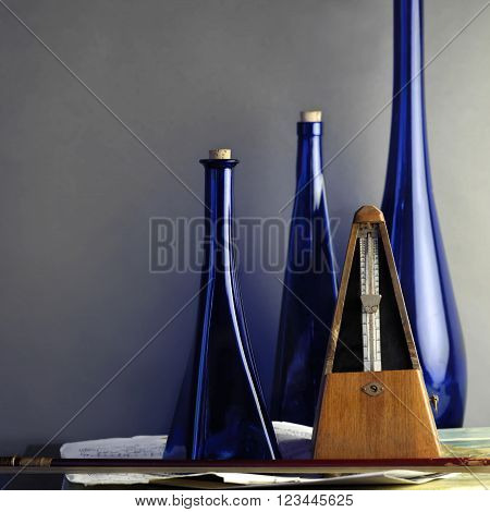 A retro metronome next to a fiddle stick and blue decorative bottles in the blurred background concept of music studio shot