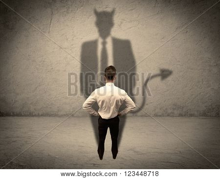 An experienced tricky businessman in suit looking at his devil desguise shadow reflected on the wall concept