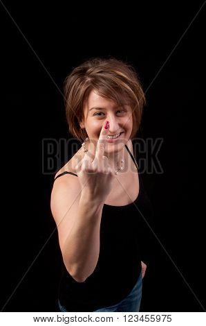 Attractive young woman making obscene hand gesture by showing middle finger on black background
