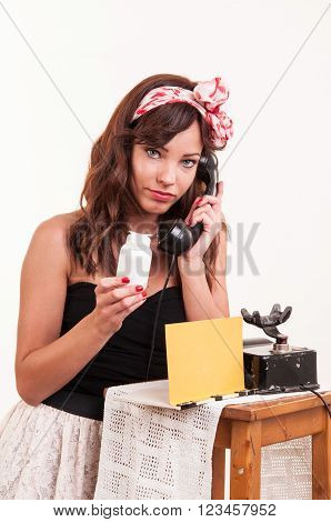 Fashion young woman with a retro look speaks at a vintage phone and looks at a bottle with medicine