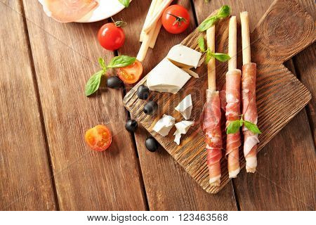 Bread sticks grissini with prosciutto ham on a  wooden board, top view
