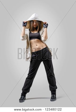 Girl dancer rejected her hip to the side holding hood of her sports jacket with both her hands.