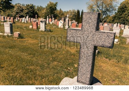 Cross in an American Cemetery with tombstones in the background and a retro effet.