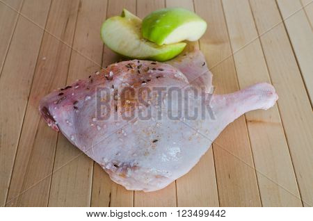 Raw duck flesh with halved, quartered apple. Raw duck meat. Spiced duck. Preparation of duck before baking on wooden background