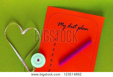 Diet plan on a red sheet of paper. List yogamat on a background of green. Measuring tape in the shape of a heart. The concept of love to a healthy lifestyle. Weight loss and fitness.
