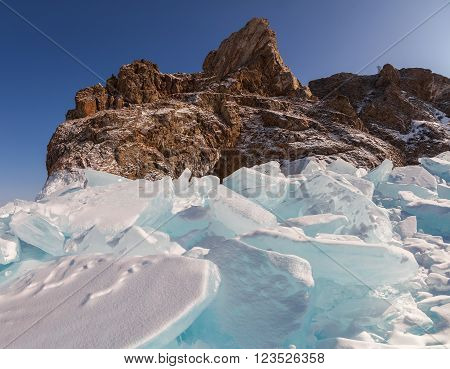 Big parts of breaking ice of The Baikal Lake in winter. High rock Khoboy on the coast