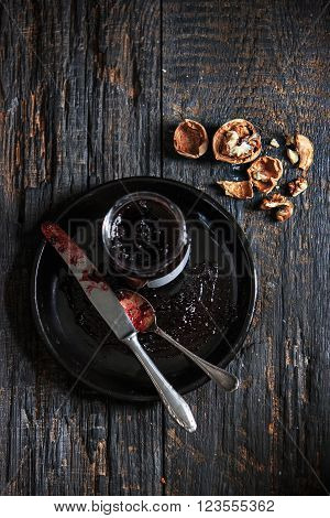 The top view of fruity jam and spoon and knife on black wooden table with walnuts