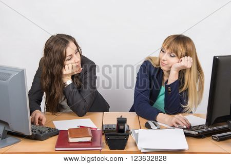 Two Young Office Employee Wearily Looking At Each Other Behind A Desk