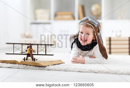 concept of children's dreams and travels. Happy pilot aviator child with a toy airplane plays at home in his room