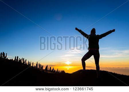 Woman hiker silhouette with arms outstretched in mountains. Female runner or climber looking at sunset view. Business concept and hands up enjoy inspirational landscape rocky trail footpath on Tenerife Canary Islands