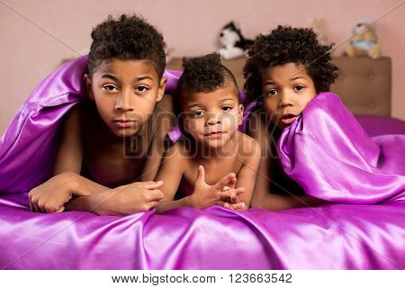 Upset afro kids under blanket. Three boys' doubtful look. We don't trust you. Troubled morning of  brothers.
** Note: Soft Focus at 100%, best at smaller sizes