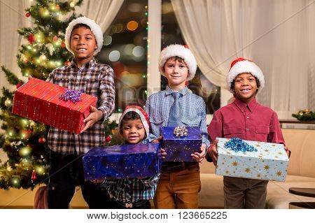 Smiling boys holding Christmas presents. Kids with presents beside spruce. Joyful holiday atmosphere at home. Let the good times roll.