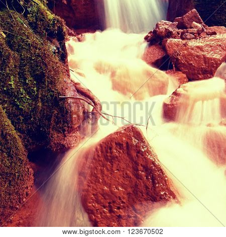 Cascades in rapid stream of mineral water. Red ferric sediments on big boulders between ferns