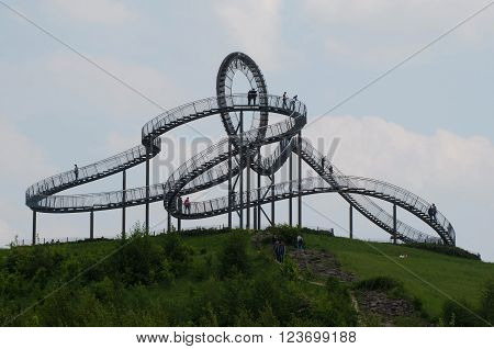 Duisburg, Germany - May 18, 2015: Tiger and Turtle Roller coaster magic Mountain with people visiting it. This sculpture is an art installation and landmark in Angerpark Duisburg 
Germany.