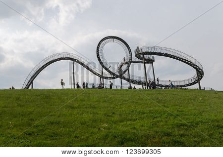 Duisburg, Germany - May 18, 2015: Tiger and Turtle Roller coaster magic Mountain with people visiting it. This sculpture is an art installation and landmark in Angerpark Duisburg 
Germany.