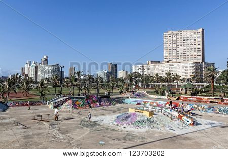 DURBAN SOUTH AFRICA - MARCH 23 2016: Many unknown childred skate boarding at colorful skate board park against city skyline on beachfront in Durban South Africa