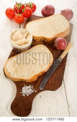 slice of bread with lard tomatoes purple onions and coarse salt on wooden board
