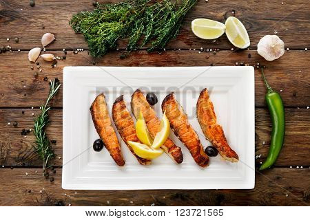 Restaurant food, salmon dish. Hot fish dish. Barbecue grilled fish dish. Restaurant food catering. Salmon barbecue grill top view with lemon and olives. Grilled salmon served in restaurant closeup.