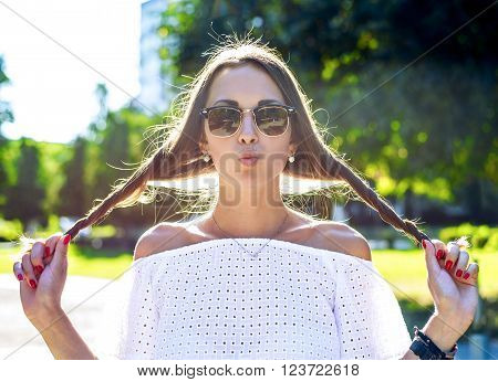 Beautiful young brunette student girl having fun with hair wearing glasses, joking kiss, resting enjoys fun, fashion style glamorous woman in a park in the summer outdoors. Close-up horizontal.