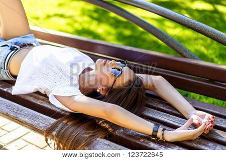 Young modern student beautiful girl, brunette lying on a park bench relaxing in the fresh air. Close-up. Happy woman.