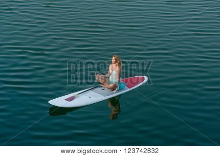 SUP bride Yoga Meditation. Girl in white dress meditating, sitting on a paddle board on water