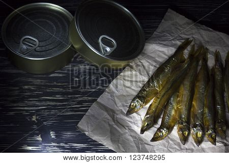 Smoked capelin and conserve tins on dark wooden background