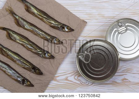 Smoked capelin and conserve tins on light wooden background