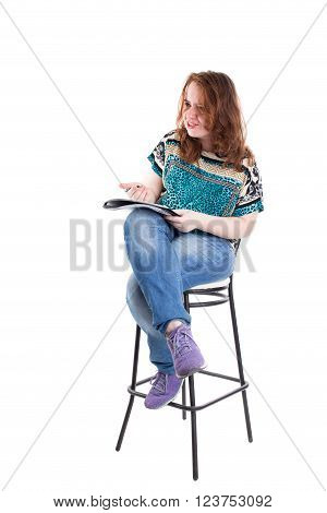Beautiful smiling redhead plus size wreckled model with folder and ballpoint pen sitting on the bar chair. Isolated on a white background.
