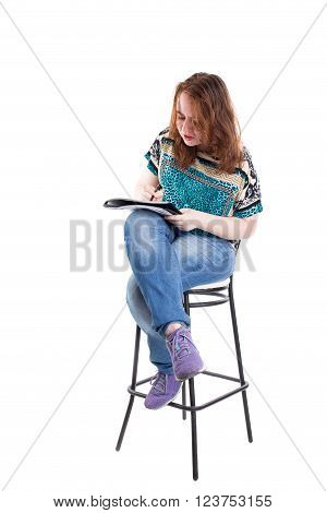 Beautiful smiling redhead plus size wreckled model with folder and ballpoint pen sitting on the bar chair. Isolated on a white background.