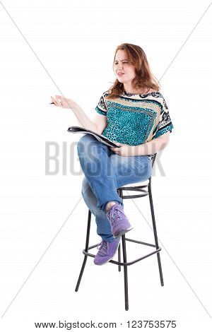 Beautiful smiling redhead plus size wreckled model with folder and ballpoint pen sitting on the bar chair. Isolated on a white background.