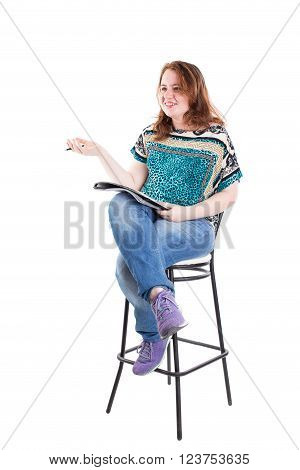 Beautiful smiling redhead plus size wreckled model with folder and ballpoint pen sitting on the bar chair. Isolated on a white background.