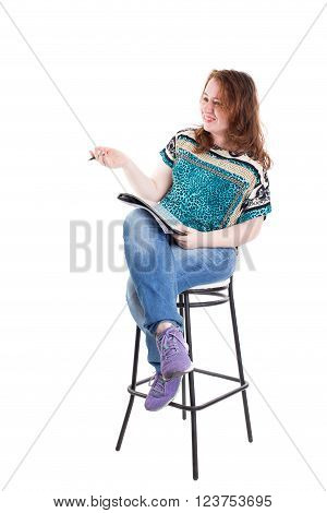 Beautiful smiling redhead plus size wreckled model with folder and ballpoint pen sitting on the bar chair. Isolated on a white background.