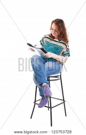 Beautiful smiling redhead plus size wreckled model with folder and ballpoint pen sitting on the bar chair. Isolated on a white background.