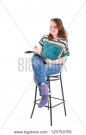 Beautiful smiling redhead plus size wreckled model with folder and ballpoint pen sitting on the bar chair. Isolated on a white background.