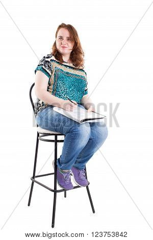 Beautiful smiling redhead plus size wreckled model with folder and ballpoint pen sitting on the bar chair. Isolated on a white background.