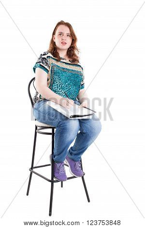 Beautiful smiling redhead plus size wreckled model with folder and ballpoint pen sitting on the bar chair. Isolated on a white background.