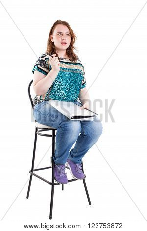 Beautiful smiling redhead plus size wreckled model with folder and ballpoint pen sitting on the bar chair. Isolated on a white background.