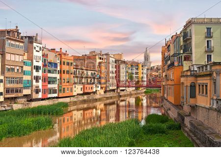 Colorful yellow and orange houses and bridge Pont de Sant Agusti reflected in water river Onyar, in Girona, Catalonia, Spain. Church of Sant Feliu and Saint Mary Cathedral at background.