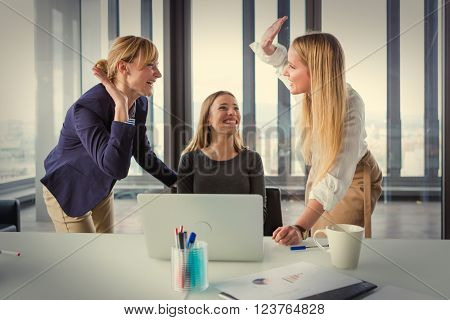 Three business women in modern office celebrating good project results. Post processed with vintage film filter.