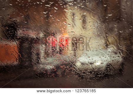 Rainy city street seen through the car windshield with focus on some water drops. Toned effect