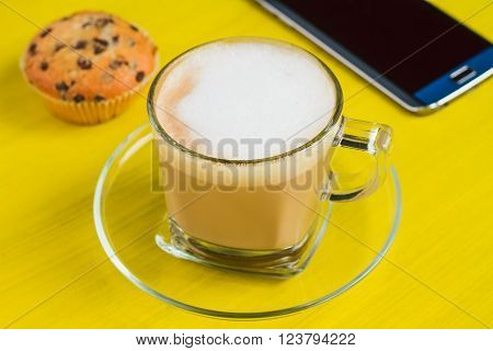 Cup of coffee on and smart phone with a blink screen on a yellow table selective focus