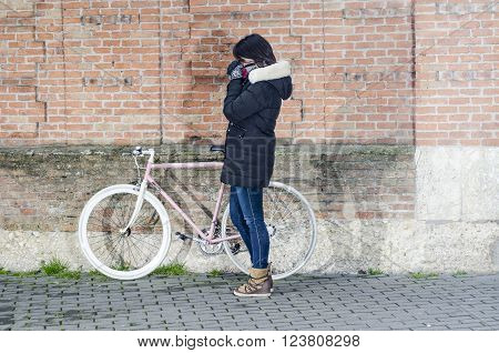 Woman with pink vintage Bicycle with white wheels leaning against a Stone Wall