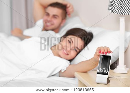 Happy couple waking up with mobile alarm clock