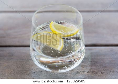 drink and refreshment concept - glass of sparkling water with lemon slices on table