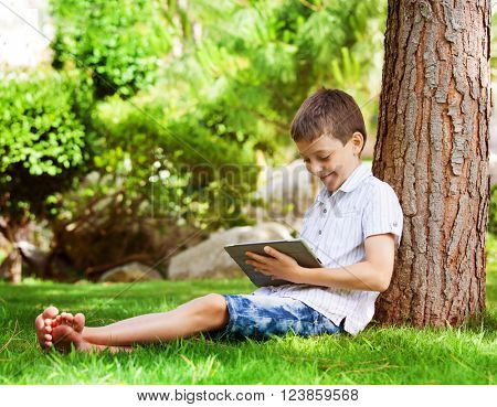 Child with tablet pc outdoors. Boy on grass with computer