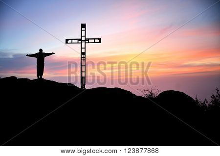 Silhouette of the man and ross on the top of the hill during colorful summer sunset. Man is thanksgiving to god.