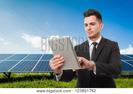 Modern businessman holding wireless tablet on solar power panels background