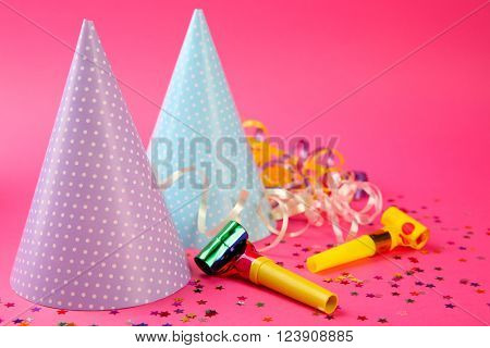 Two dotted Birthday hats with serpentine streamer and noise makers on pink background