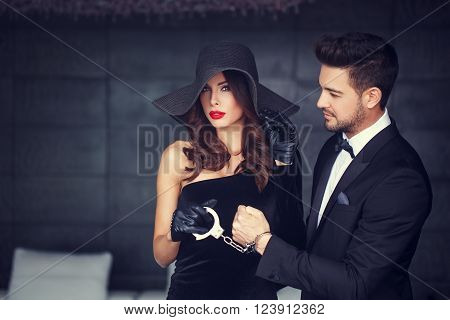 Sexy woman in hat holding macho man on handcuffs, bdsm